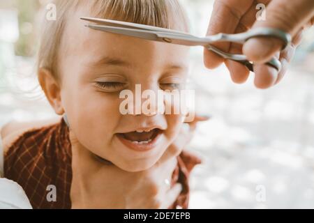 Première coupe de cheveux du petit garçon à la maison par les parents. Joli portrait amusant. Banque D'Images