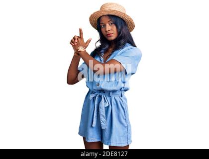 Jeune fille indienne portant un chapeau d'été tenant un pistolet symbolique avec un geste de main, jouant tuant des armes de tir, visage en colère Banque D'Images