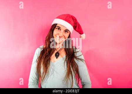 Jolie jeune fille avec des taches de rousseur et portant un chapeau de père Noël, regardant l'appareil photo détendu et serein, isolé sur fond rose féminin et espace de copie. Banque D'Images