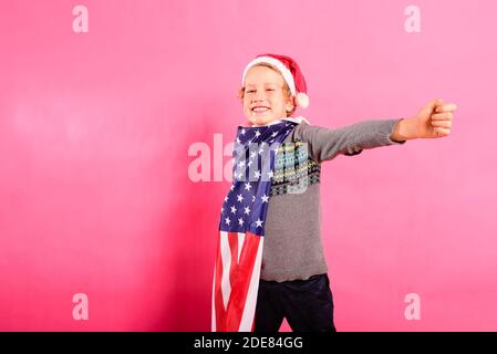 Un garçon américain célèbre Noël avec un grand sourire, isolé sur fond de drapeau américain. Banque D'Images