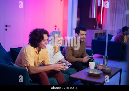 Meilleurs amis assis à la maison pendant une soirée agréable et jouant à des jeux sur la console. Ils se défient mutuellement pour gagner. Banque D'Images