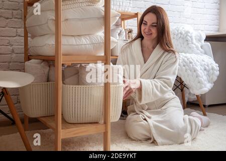 Jeune femme en robe chaude est d'organiser le placard de linge avec des serviettes, draps et couvertures soigneusement pliés. Banque D'Images