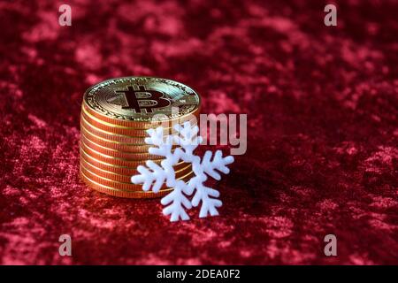 Pile de bitcoins d'or sur fond de velours rouge, avec flocons de neige blancs Banque D'Images