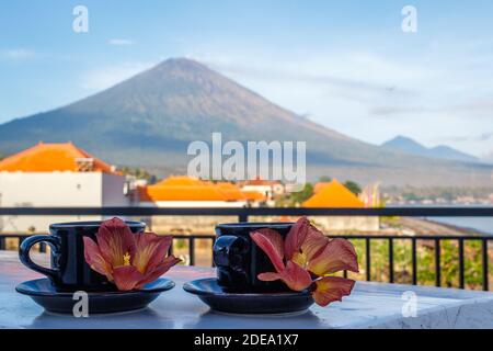 Two cups of coffee with flowers of Hibiscus Tiliaceus or Sea hibiscus, view of volcano Agung on the background. Amed, Karangasem, Bali, Indonesia. Stock Photo