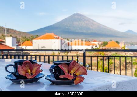 Two cups of coffee with flowers of Hibiscus Tiliaceus or Sea hibiscus, view of volcano Agung on the background. Amed, Karangasem, Bali, Indonesia. Stock Photo