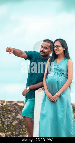 Un jeune couple, mari pointant vers quelque chose au loin, une belle femme enceinte avec un sourire mignon, portrait debout dans la lumière naturelle, et gr Banque D'Images