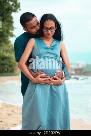 Les jeunes parents s'attendent à ce que leur nouveau-né porte le ventre de leur mère dans les deux mains et un léger baiser dans le cou. Photo de près à l'avant sous des lumières naturelles à l'intérieur Banque D'Images