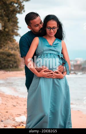 Les jeunes parents s'attendent à ce que leur nouveau-né porte le ventre de leur mère dans les deux mains et un léger baiser dans le cou. Photo de près à l'avant sous des lumières naturelles à l'intérieur Banque D'Images