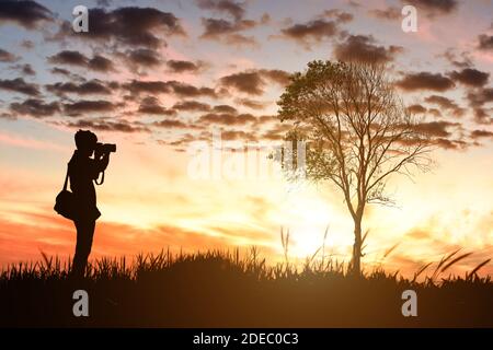 Silhouette de photographe masculin prenant des photos sur fond de coucher de soleil. Banque D'Images