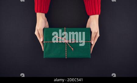 Femme mains donnant vert christsma boîte cadeau vue dessus arrière-plan noir Banque D'Images