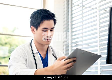 Portrait d'un jeune homme attrayant médecin asiatique passant par sa liste médicale dans son bureau. Banque D'Images