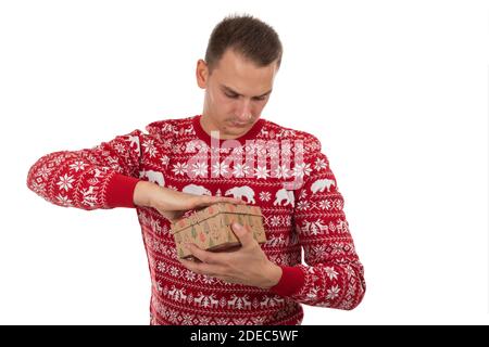 Beau jeune homme avec tricots de noël rouges tenant un cadeau boîte sur isolé Banque D'Images