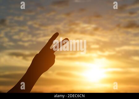 Silhouette de main montrant deux doigts sur fond de coucher de soleil. Banque D'Images