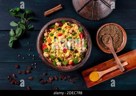 Couscous traditionnel dans un tajine, tiré du dessus avec des épices et des herbes sur un fond en bois sombre Banque D'Images