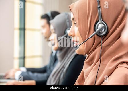 Femme musulmane portant un micro-casque travaillant comme opérateur de service à la clientèle avec l'équipe dans le bureau du centre d'appels Banque D'Images