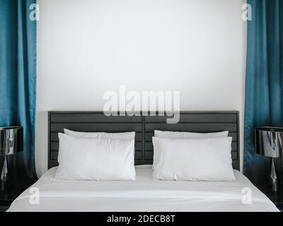 Oreillers blancs et propres pour le couple sur le lit dans la chambre à l'hôtel avec espace blanc de fond de mur entre le rideau bleu. Banque D'Images