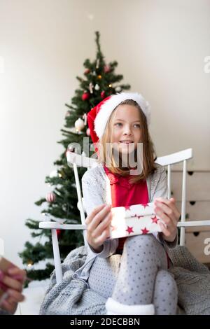 Jolie fille dans santa clause chapeau devant un Arbre de Noël avec cadeaux de Noël Banque D'Images