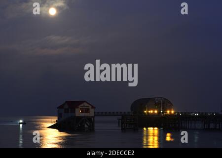 Pleine lune se reflétant sur la mer à Mumbles. La jetée, la station de Lifeboat et un bateau de pêche sont éclairés par le clair de lune et les derniers rayons du soleil couchant. Banque D'Images