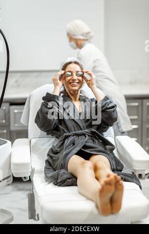 Jeune femme se préparant à un traitement de rajeunissement, portant des lunettes de protection au bureau de SPA médical avec un médecin en arrière-plan Banque D'Images