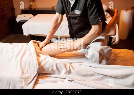 Thérapeute professionnel effectuant un massage profond à un client masculin au Spa salon. Travaillant sur le corps inférieur Banque D'Images