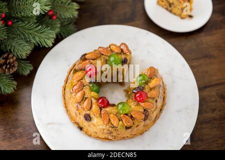 Gâteau de Noël creux rond glacé recouvert d'amandes et de glace cerises sur plaque blanche à côté des aiguilles de pin vert table en bois Banque D'Images
