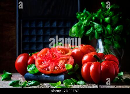 Grosses tomates rouges avec feuilles de basilic vert sur le fond en bois ancien, foyer sélectif Banque D'Images