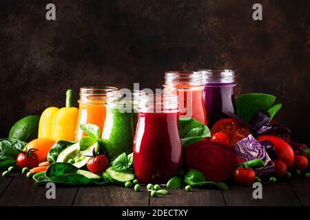 Jus de légumes végétaliens multicolores et smoothies de tomate, carotte, poivre, chou, épinards, betterave en bouteilles de verre sur table de cuisine rustique, ve Banque D'Images