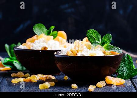 Fromage cottage maison avec abricots séchés, raisins secs et menthe dans des bols d'argile, petit déjeuner sain, fond sombre, foyer sélectif Banque D'Images