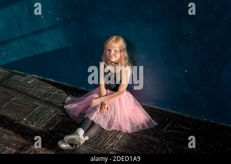 Jolie petite fille blonde en tutu rose et chaussures pointe assis sur le gloor et le repos takin après l'entraînement de danse de ballet en classe studio Banque D'Images