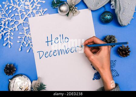 Bonjour décembre. La main de la fille écrit le texte sur une feuille blanche de papier. Composition de Noël. Banque D'Images