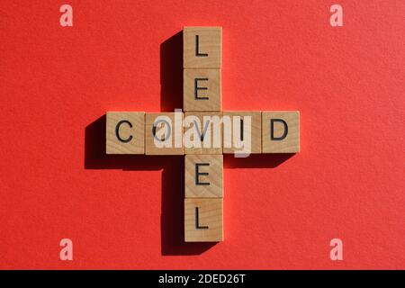 Covid, niveau, mots en lettres de l'alphabet en bois en forme de mots croisés isolés sur fond rouge Banque D'Images