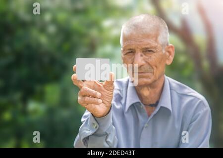 Un vieil homme souriant montrant une carte de débit ou de crédit vierge en mettant l'accent sur la carte de crédit en regardant directement l'appareil photo Banque D'Images