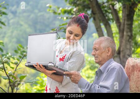 Jeune femme indienne aidant son vieux père à la retraite sur un ordinateur portable assis à l'extérieur de la maison de village rurale. Banque D'Images