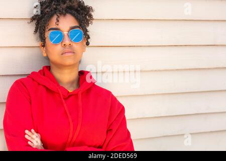 Fille adolescente cool adolescent mixte race biracial Afro-américaine femelle jeune femme portant des lunettes de soleil reflétant l'avion aérien dans le ciel bleu dedans soleil d'été Banque D'Images