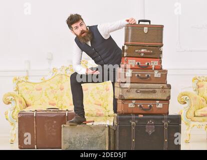 L'homme, barbe et moustache avec butler offre une assurance, luxe intérieur blanc arrière-plan. Élégant Macho sur choqué face debout près de tas de vintage suitcase. Assurance et voyager concept. Banque D'Images