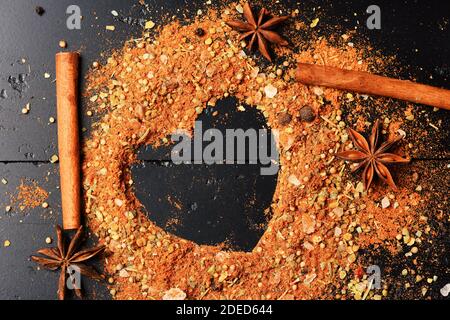 Concept de l'art alimentaire. Ensemble d'épices sur fond de texture gris foncé. Bâtonnets de cannelle et étoiles d'anis sur un assaisonnement parsemé. Composition du condiment pour une silhouette en forme de coeur Banque D'Images