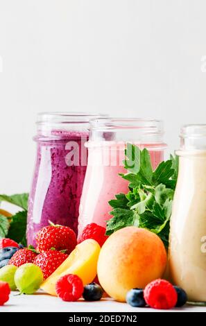 Smoothies aux baies colorées, sains et utiles, avec yaourt, fruits frais et baies sur fond gris, sélectif Banque D'Images