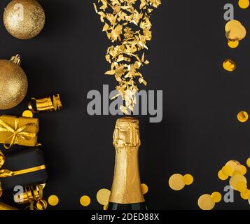 Une bouteille de champagne dorée déborde d'or dans le cadre d'or festive décoration de Noël boules confetti cadeaux sur fond noir. Flat Lay Nouveau Banque D'Images