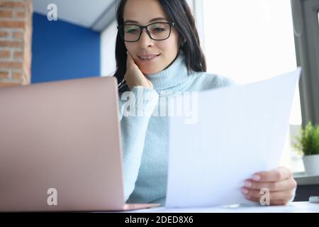 Femme avec des lunettes pour ranger des documents et travailler sur un ordinateur portable. Banque D'Images
