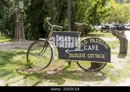 Un vélo avec des panneaux pour les attractions touristiques locales à Arrowtown en Nouvelle-Zélande pour la location de vélos, Dudweys Cottage et la recherche d'or Banque D'Images