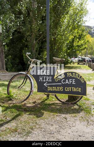 Un vélo avec des panneaux pour les attractions touristiques locales à Arrowtown en Nouvelle-Zélande pour la location de vélos, Dudweys Cottage et la recherche d'or Banque D'Images