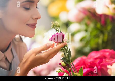 Joyeux fleuriste femelle aux yeux fermés qui sent la fleur d'eustoma avec fleurs floues en arrière-plan Banque D'Images