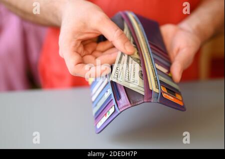 les mains des hommes tiennent des billets de 100 dollars et un portefeuille sur une table grise Banque D'Images