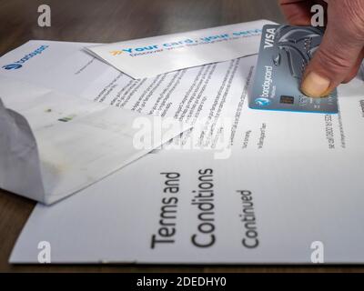 Main d'un homme tenant une nouvelle carte de crédit Barclaycard, collée à la lettre d'accompagnement, et entourée de termes et conditions et d'autres documents. Banque D'Images