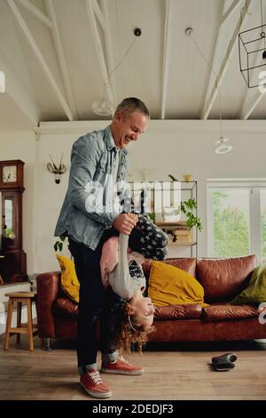 Père jouant avec la fille la portant à l'envers à la maison Banque D'Images