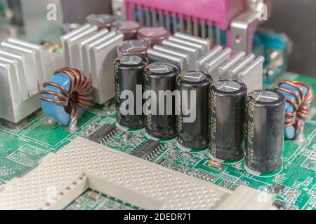 Gros plan d'une rangée de 5 condensateurs électrolytiques électriques en aluminium sur une carte mère d'ordinateur (pcb) imprimée en vert. Ailettes de refroidissement en aluminium. Banque D'Images