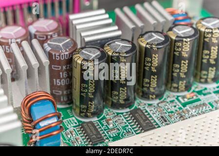 Gros plan d'une rangée de 5 condensateurs électrolytiques électriques en aluminium sur une carte mère d'ordinateur (pcb) imprimée en vert. Ailettes de refroidissement en aluminium. Banque D'Images