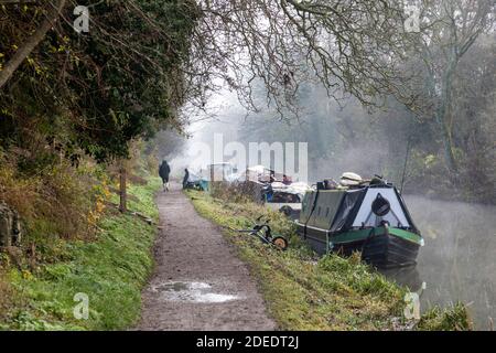 Marcheur au bord du canal des bateaux amarrés à côté du chemin de halage du canal Kennet et Avon lors d'une journée d'hiver brumeuse. Bradford on Avon, Wiltshire, Angleterre, Royaume-Uni Banque D'Images