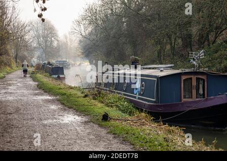 Marcheur au bord du canal des bateaux amarrés à côté du chemin de halage du canal Kennet et Avon lors d'une journée d'hiver brumeuse. Bradford on Avon, Wiltshire, Angleterre, Royaume-Uni Banque D'Images