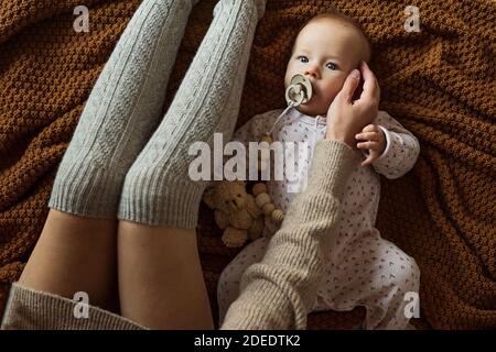 Adorable petite fille caucasienne couchée sur un lit confortable avec sa mère vêtue d'un chandail tricoté de couleur brune. Restez à la maison pendant la quarantaine du coronavirus covid-19 Banque D'Images